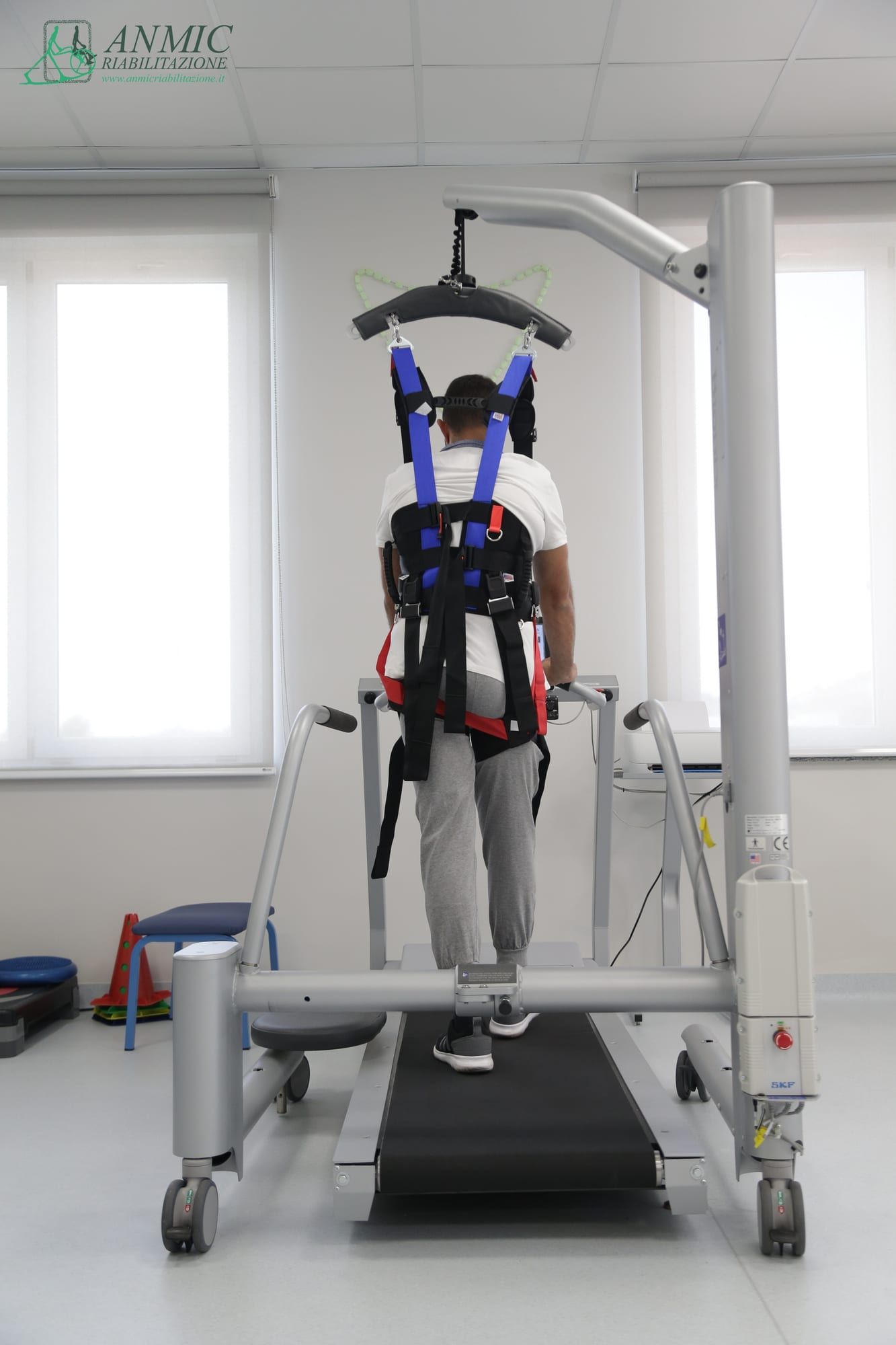 Paziente su treadmill con imbracatura di sostegno durante una seduta di rieducazione del cammino